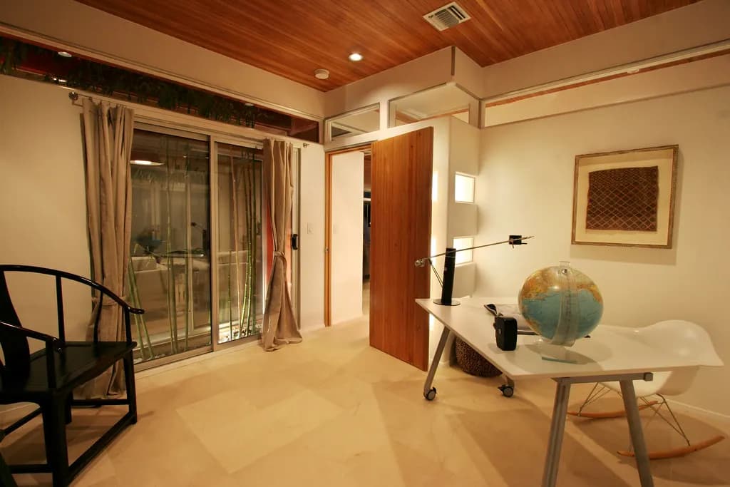 A finished home office with a timber-panelled ceiling, recessed lights, stone floor tiles, a white desk and a wooden door