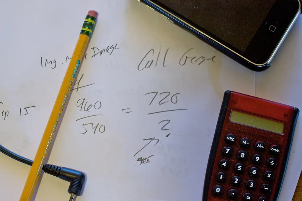 Handwritten calculations on paper next to a pencil, a calculator and a phone