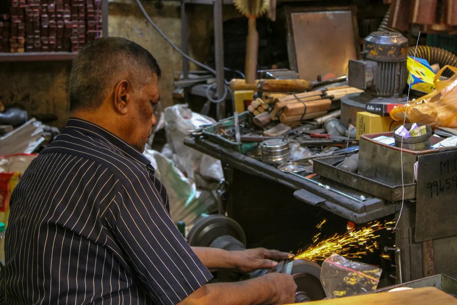 A metalworker operating a machine in a small workshop on Market Road, Mysuru, Karnataka