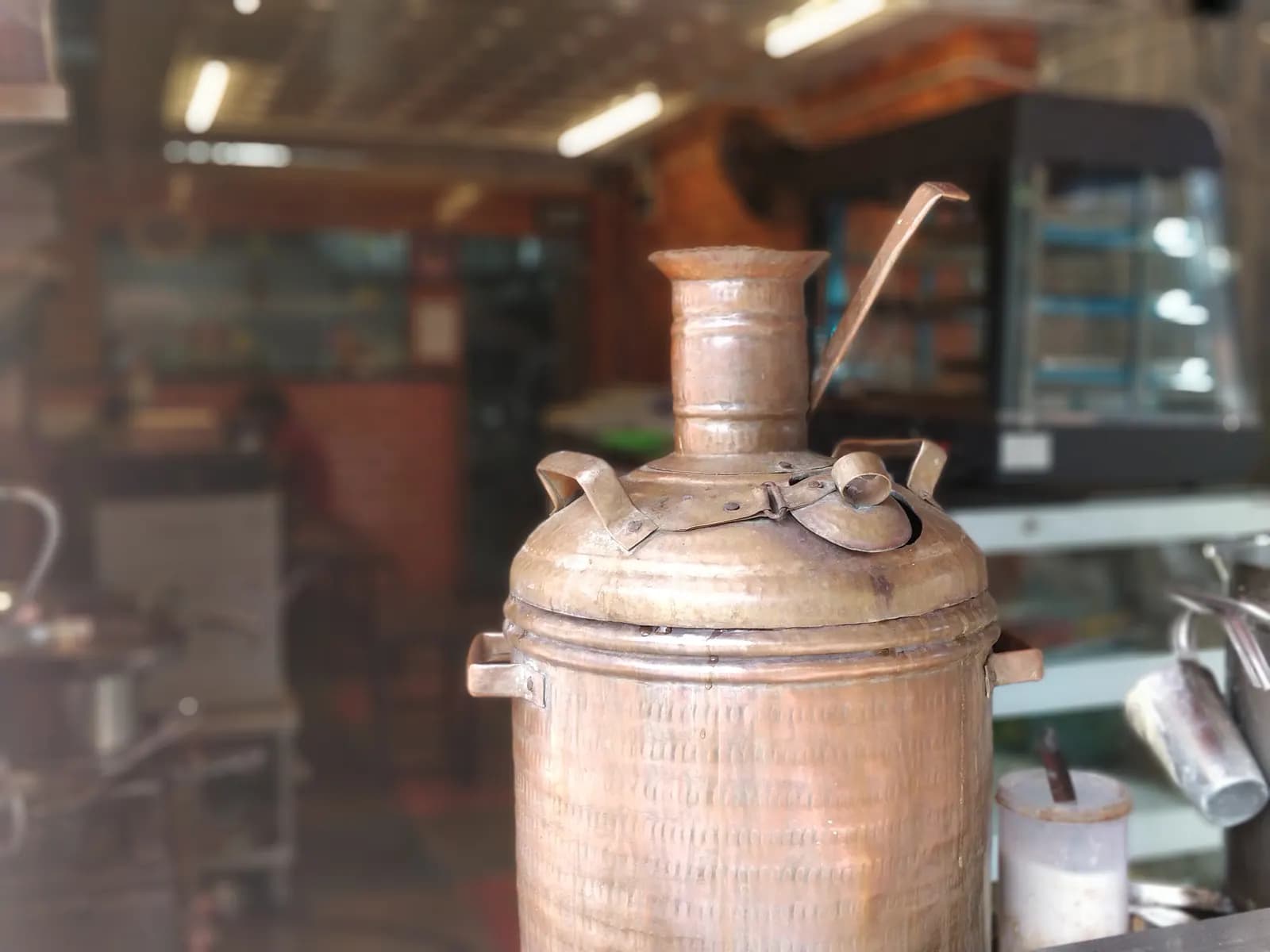 A copper samovar on the counter of a small tea shop in Bengaluru, with the shop's display cabinet behind it