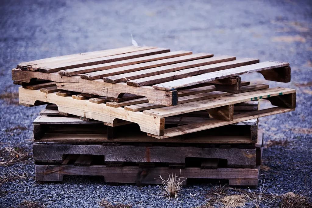 A stack of used wooden pallets on gravel outside a warehouse