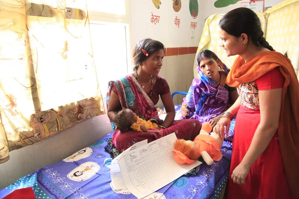 A health worker talks with two mothers holding their babies at a health centre in India