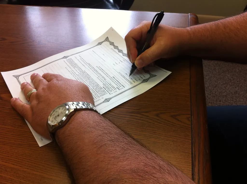 A hand signing a printed agreement with a pen on a wooden table
