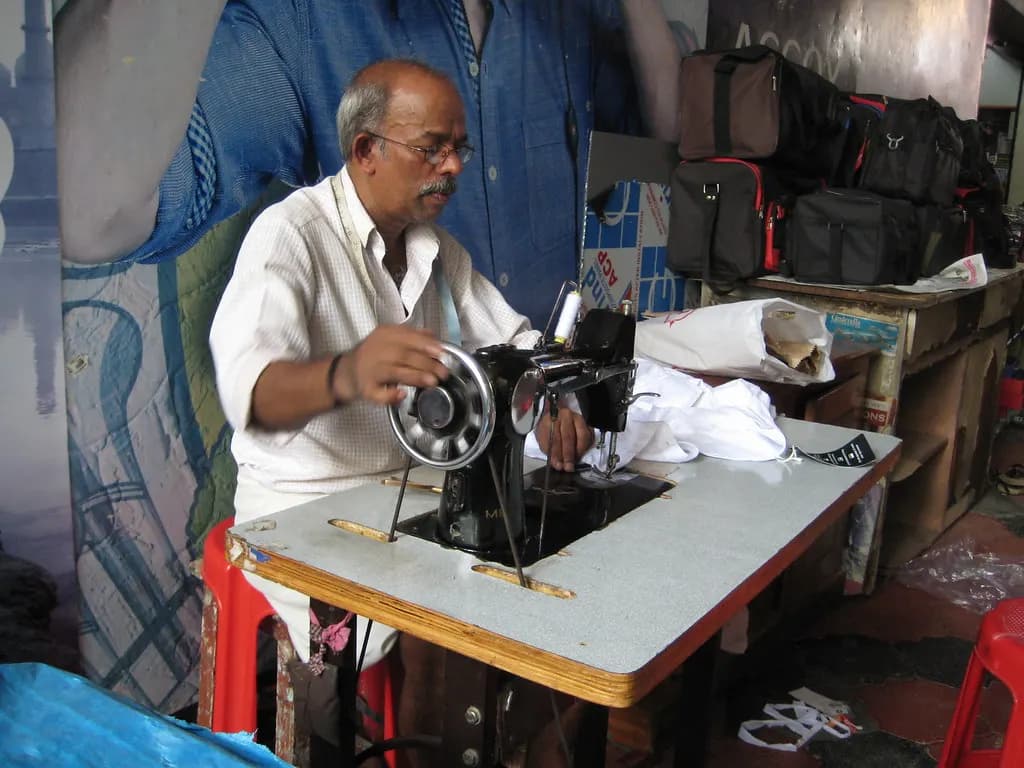 A tailor working at a treadle sewing machine in a small shop in Attingal, Kerala