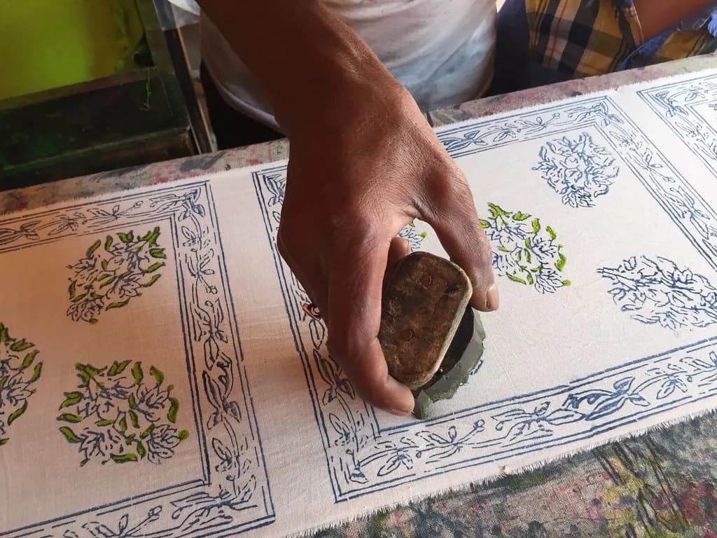 A worker pressing a carved wooden block onto cotton fabric during hand block printing in Jaipur
