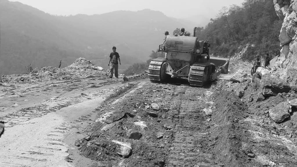 A bulldozer cutting a mountain road in Sikkim, with a worker standing nearby