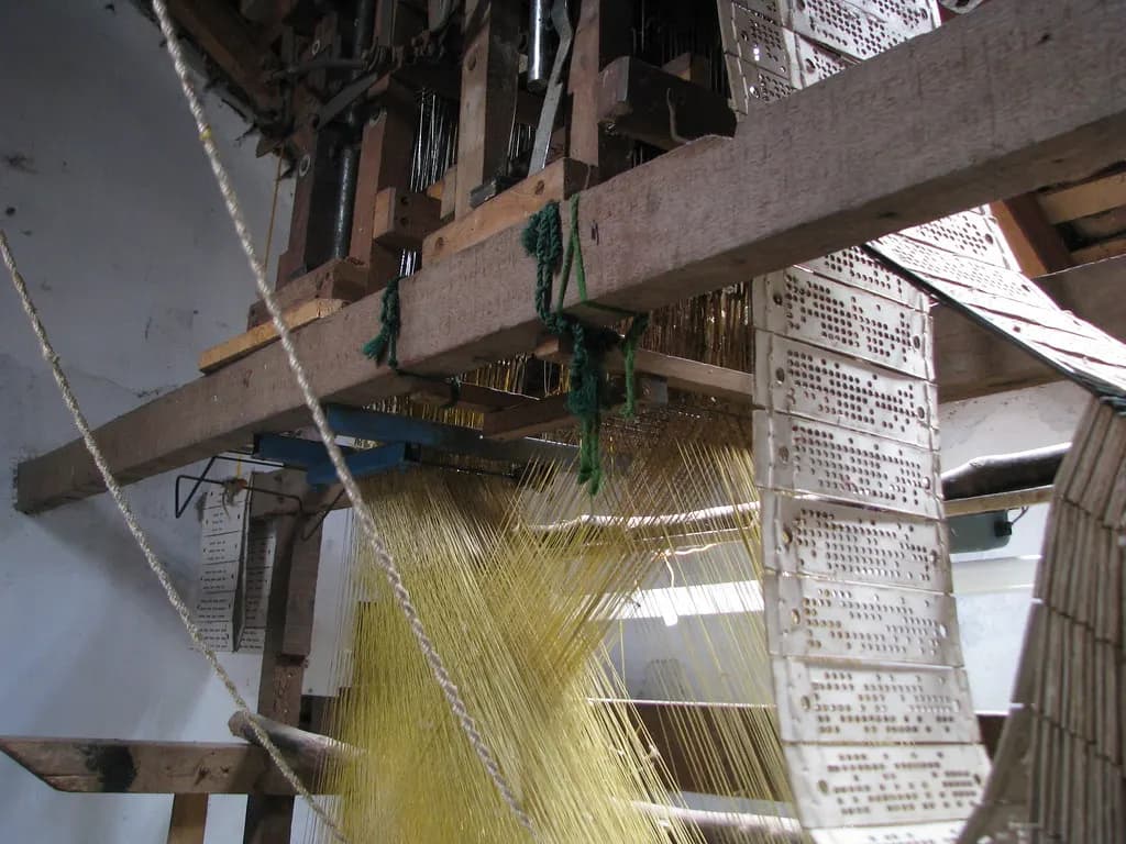 A wooden jacquard handloom with punched pattern cards and yellow silk warp threads in an Indian weaving workshop
