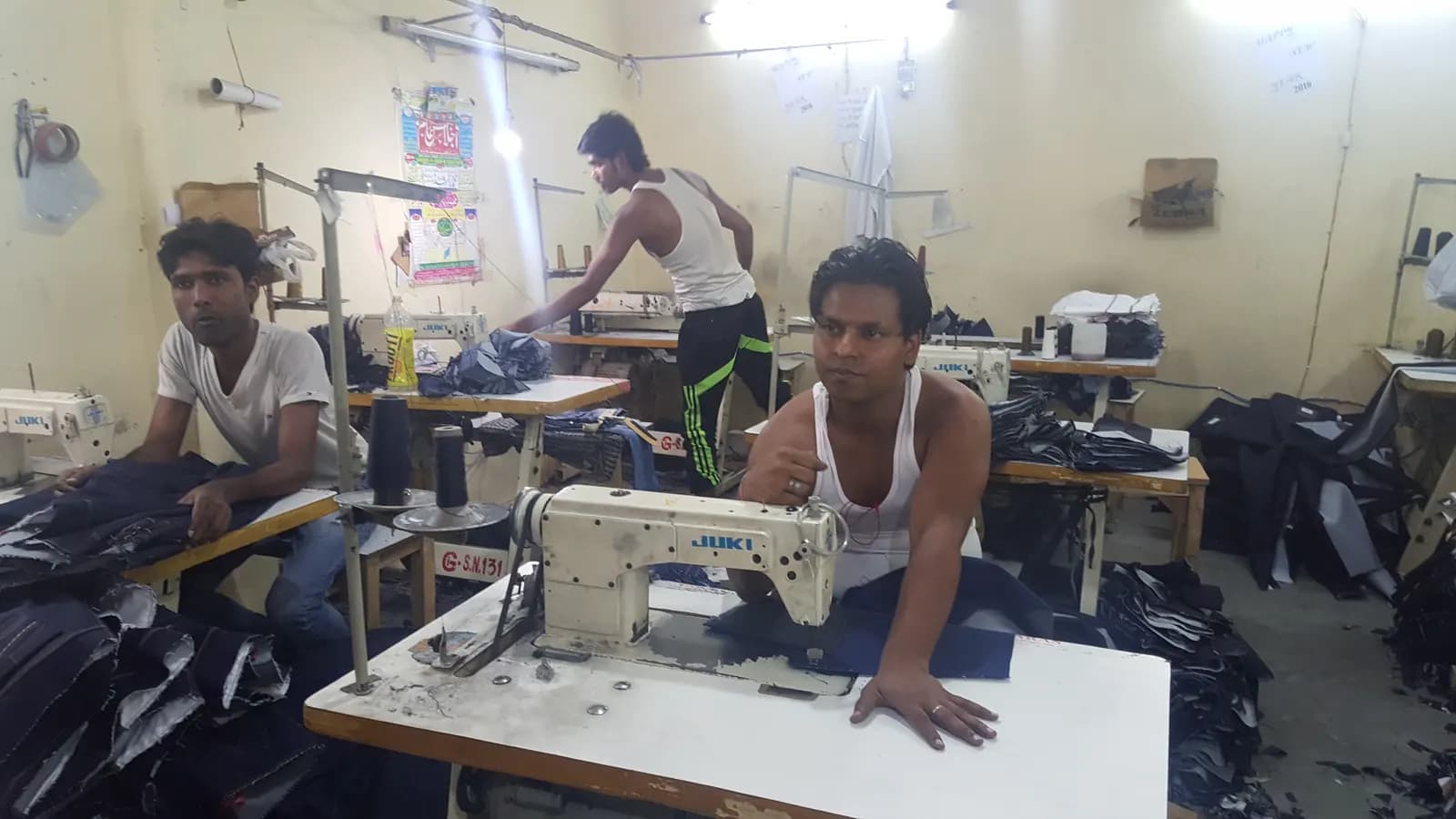 Tailors working at sewing machines in a small garment unit in Karawal Nagar, Delhi