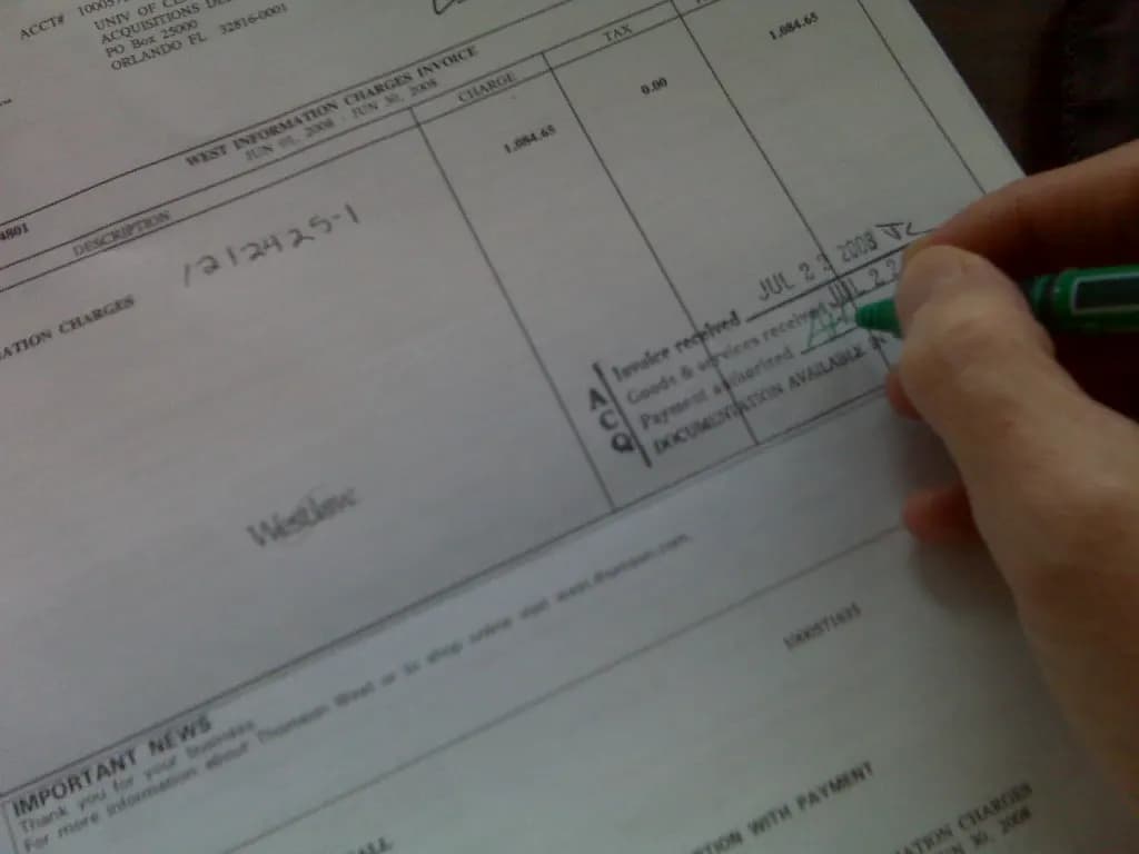 A hand initialling the goods-received and invoice-received stamp on a printed invoice