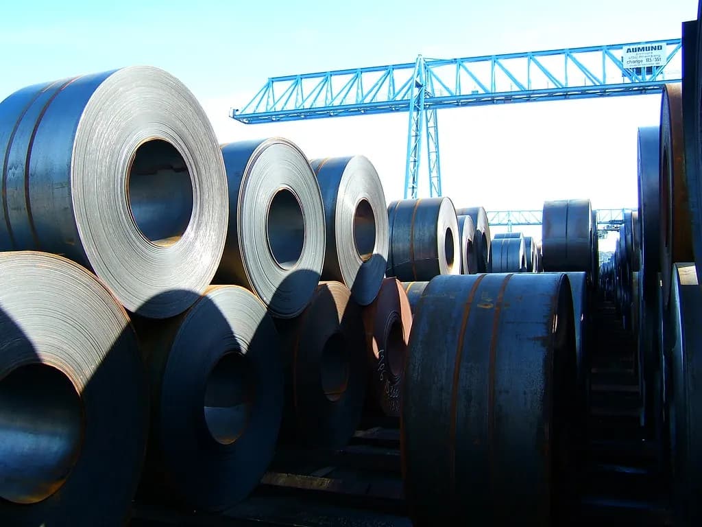 Stacks of rolled steel coils in a storage yard under a gantry crane