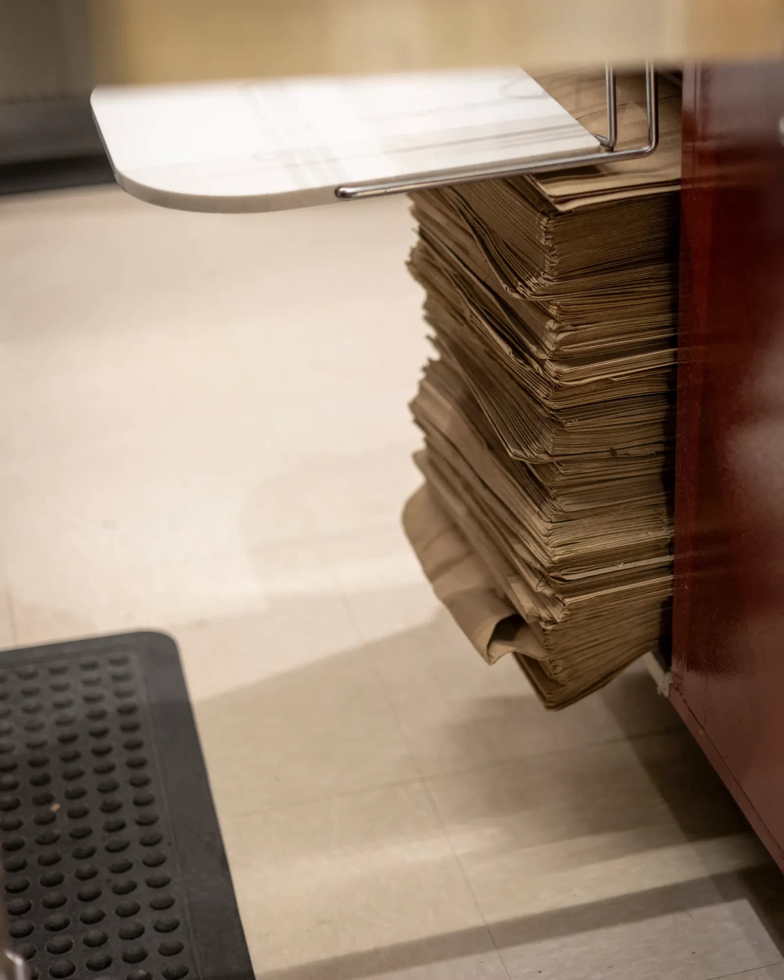 A stack of plain brown kraft paper bags stored beneath a shop counter