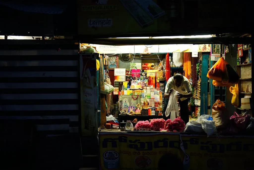 A small Indian general store lit up at night, its shelves stocked with goods