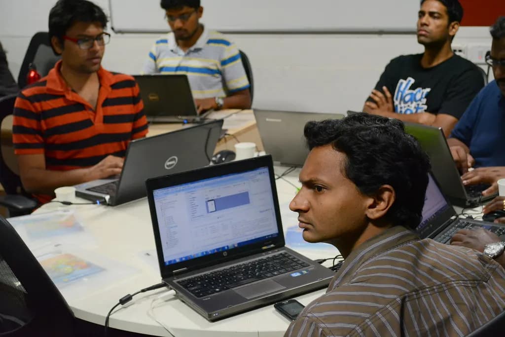 Young salaried professionals working on laptops around a table in an Indian office