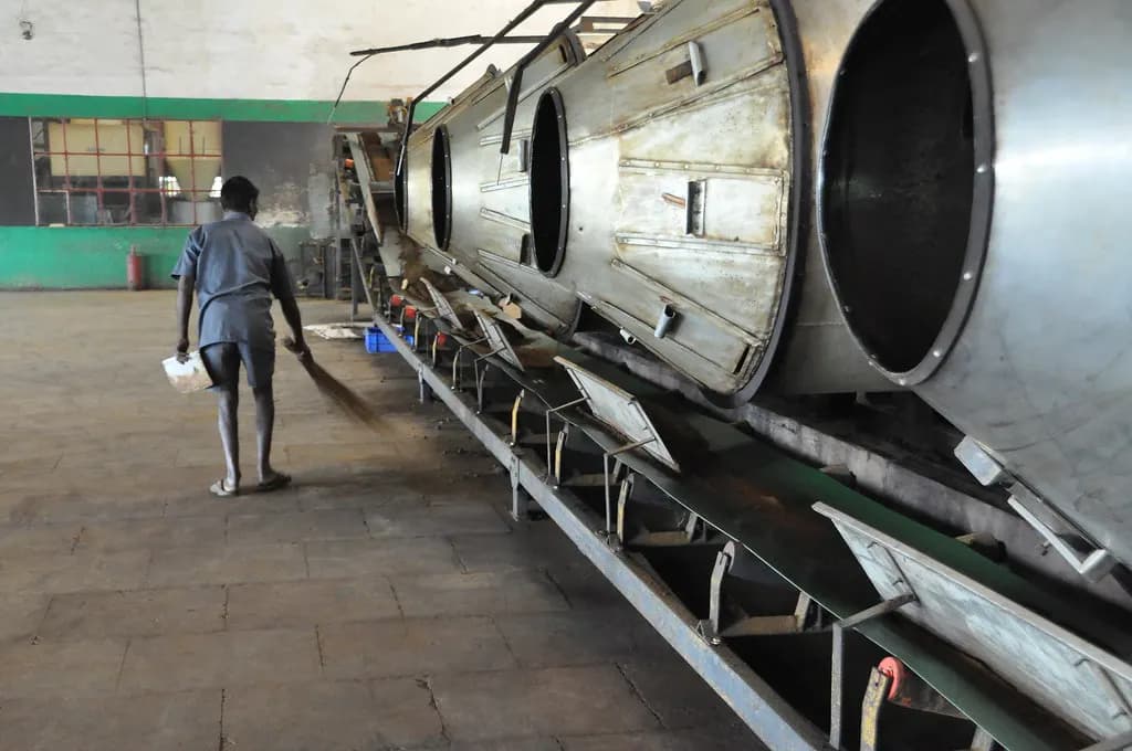 A worker sweeping the floor beside processing machines in an Indian tea factory
