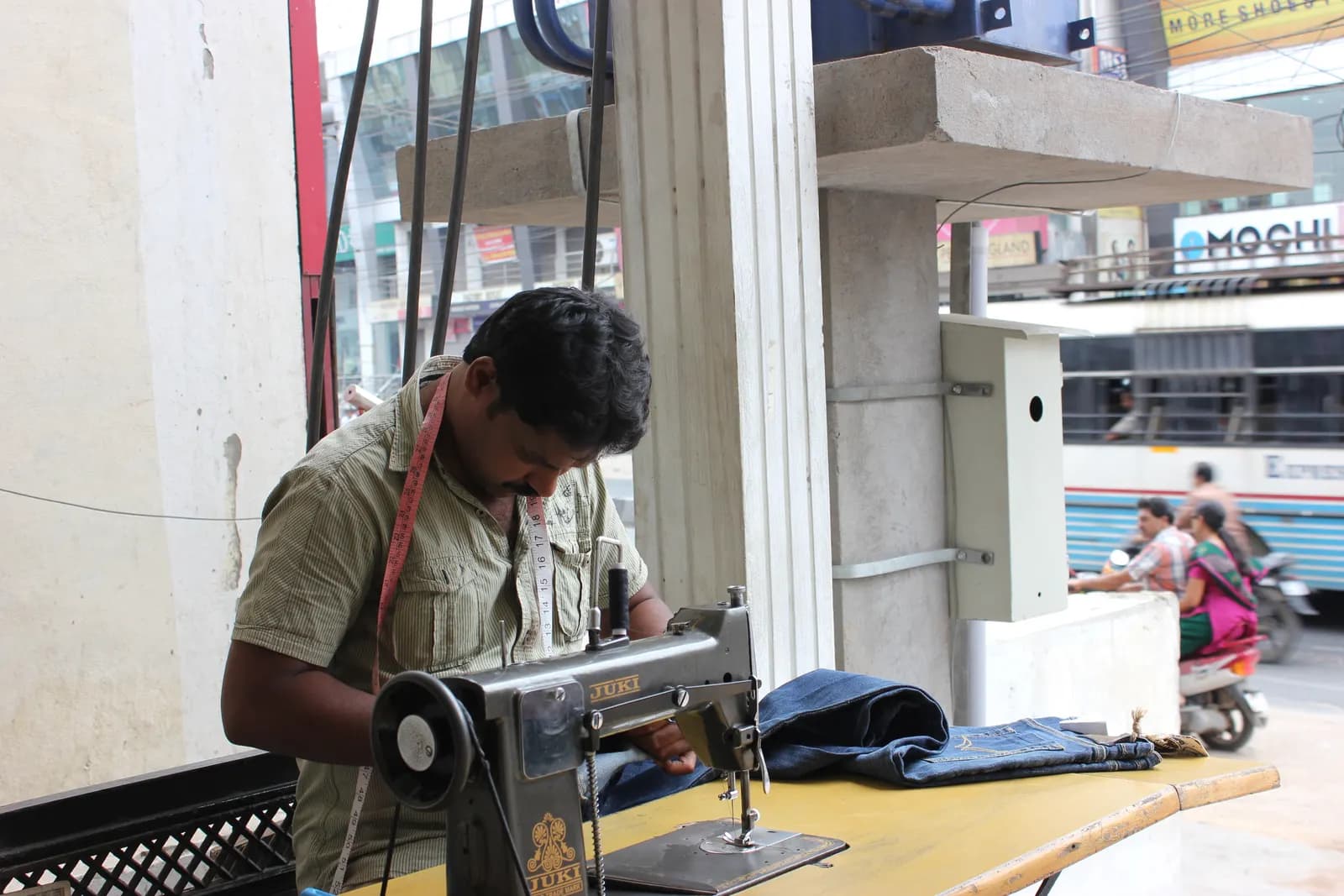 A tailor stitching denim on a manual sewing machine at a roadside shop in India