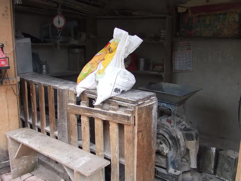 A small neighbourhood flour mill in India with a grinding machine, weighing scale and sacks of grain