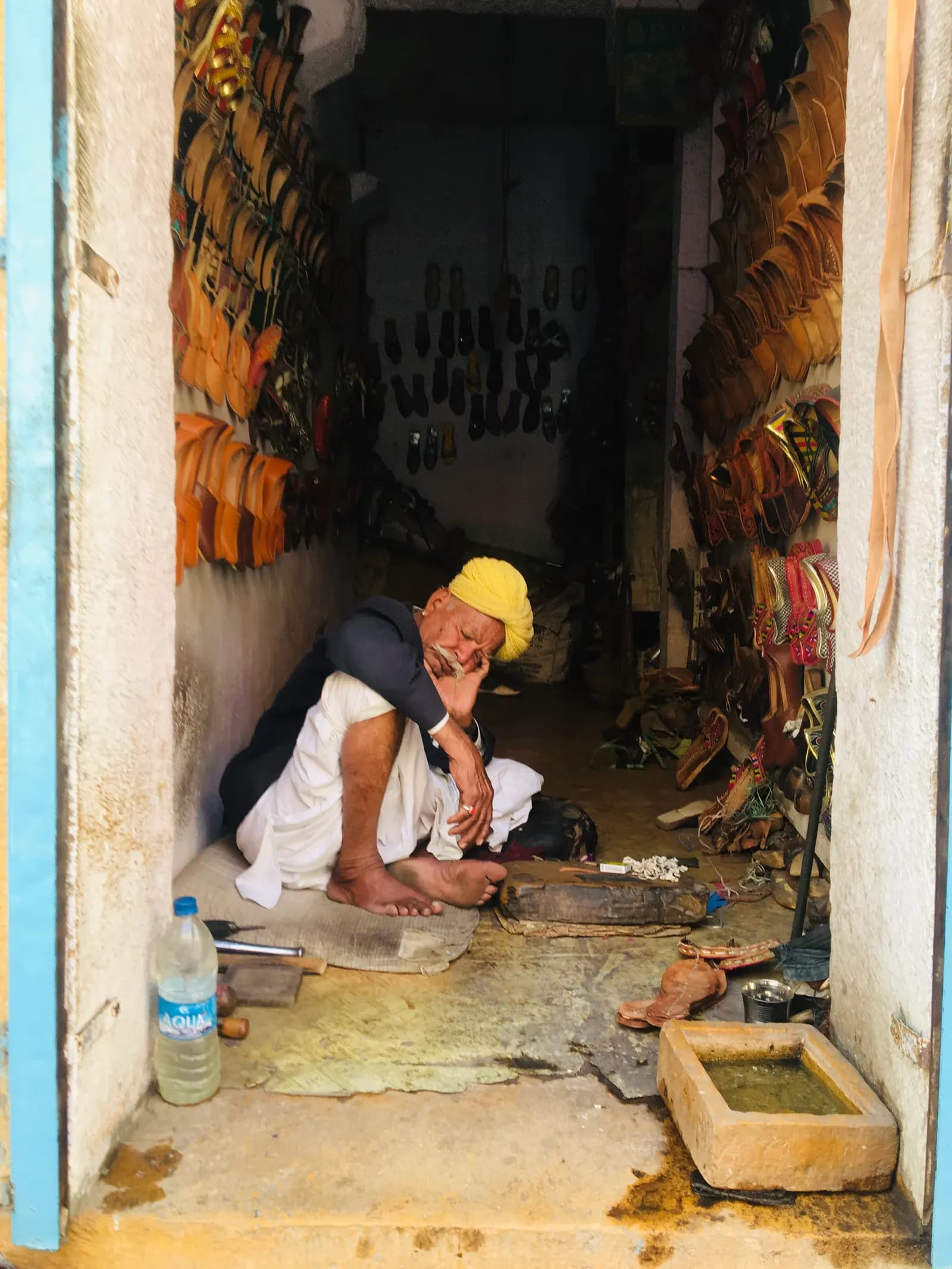 A shoemaker sitting in his narrow workshop in Jaisalmer, with handmade leather footwear hanging on both walls