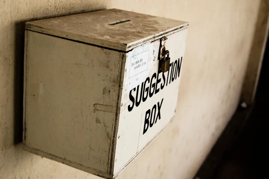 A wooden suggestion box with a padlock mounted on a wall
