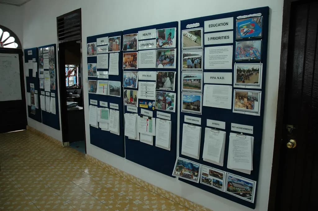 Notice boards with printed notices and photographs pinned along an office corridor wall