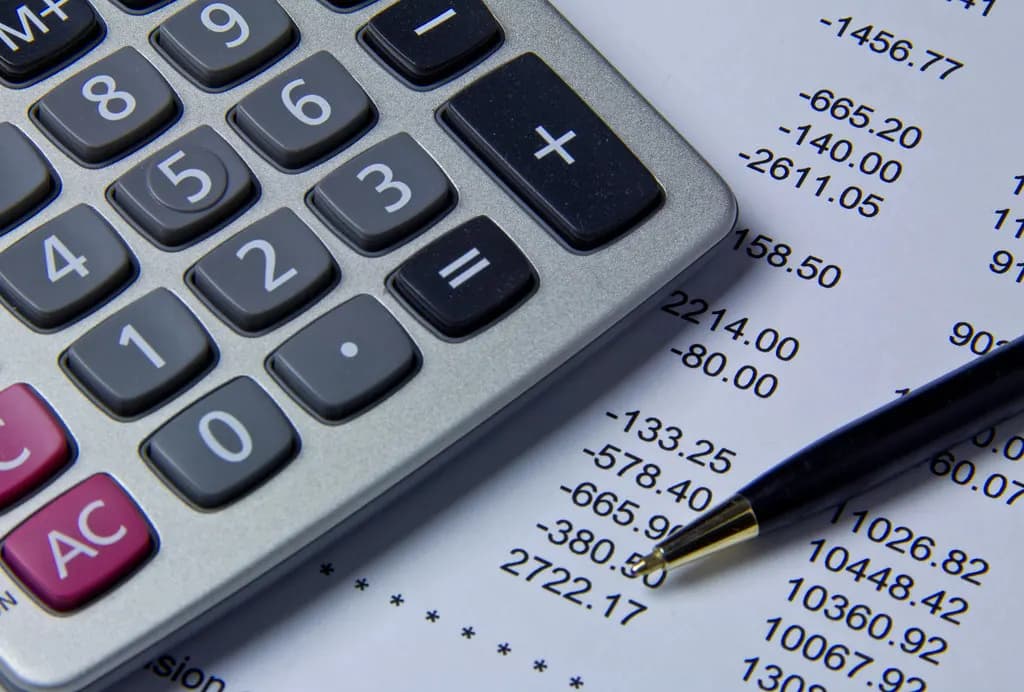 A calculator beside a printed ledger of figures with a pen, used to balance business accounts