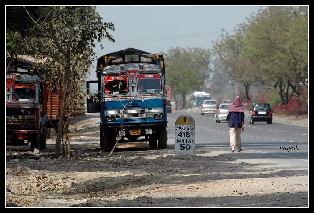 A brightly painted goods truck parked beside a national highway milestone in India