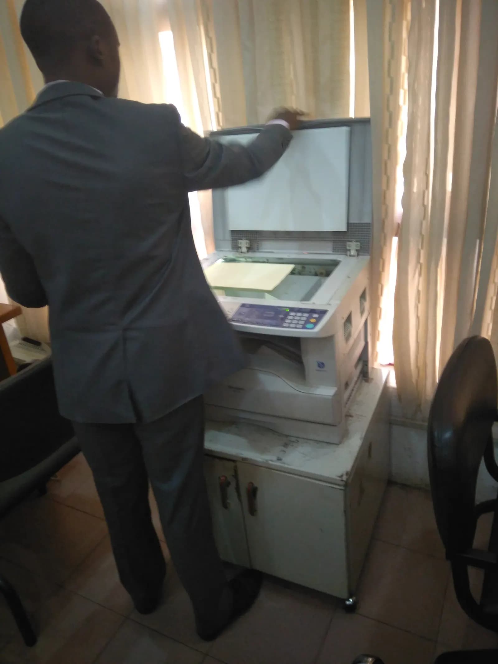 A man in a suit making copies on an office photocopier standing on a cabinet in a small photocopy shop