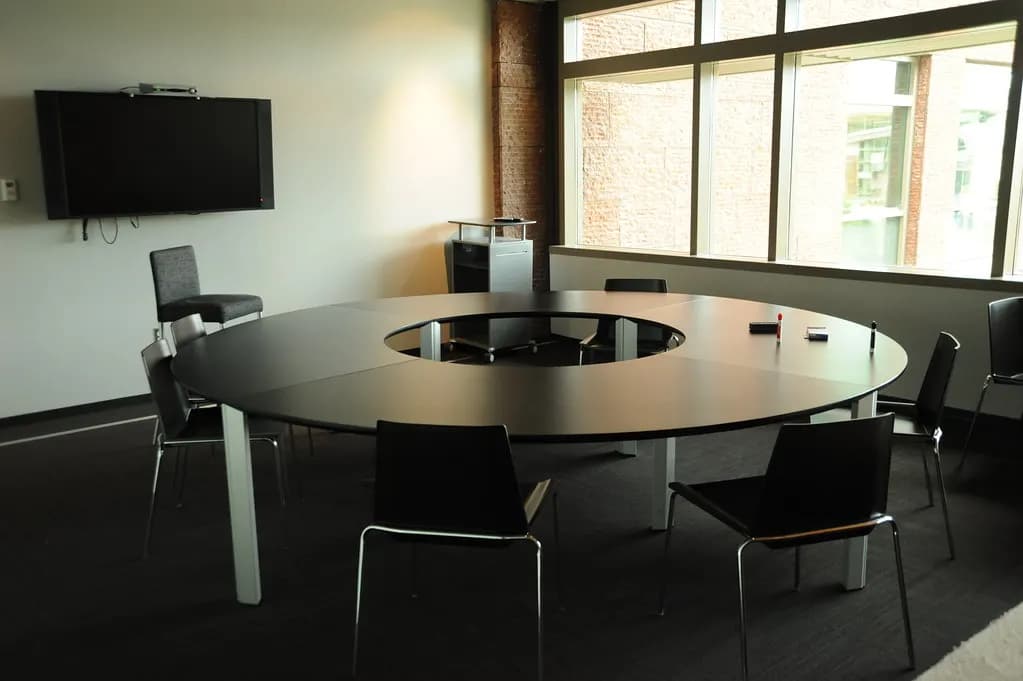 A round conference table with chairs and a wall-mounted screen in an office meeting room