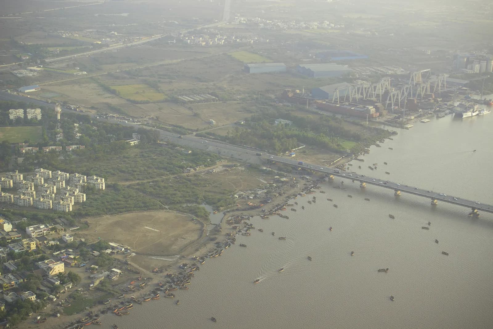Aerial view of Surat's outskirts on the Tapi estuary, with a road bridge, housing blocks, factory sheds and a shipyard