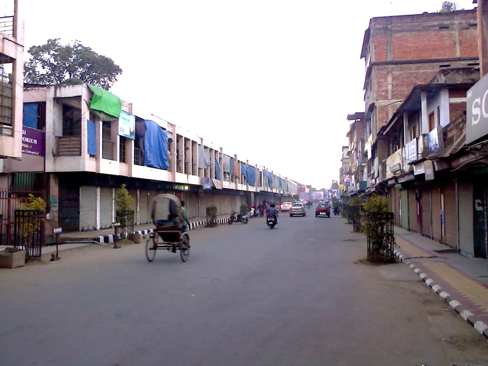 A quiet street in Imphal lined with two- and three-storey shop buildings and a cycle-rickshaw