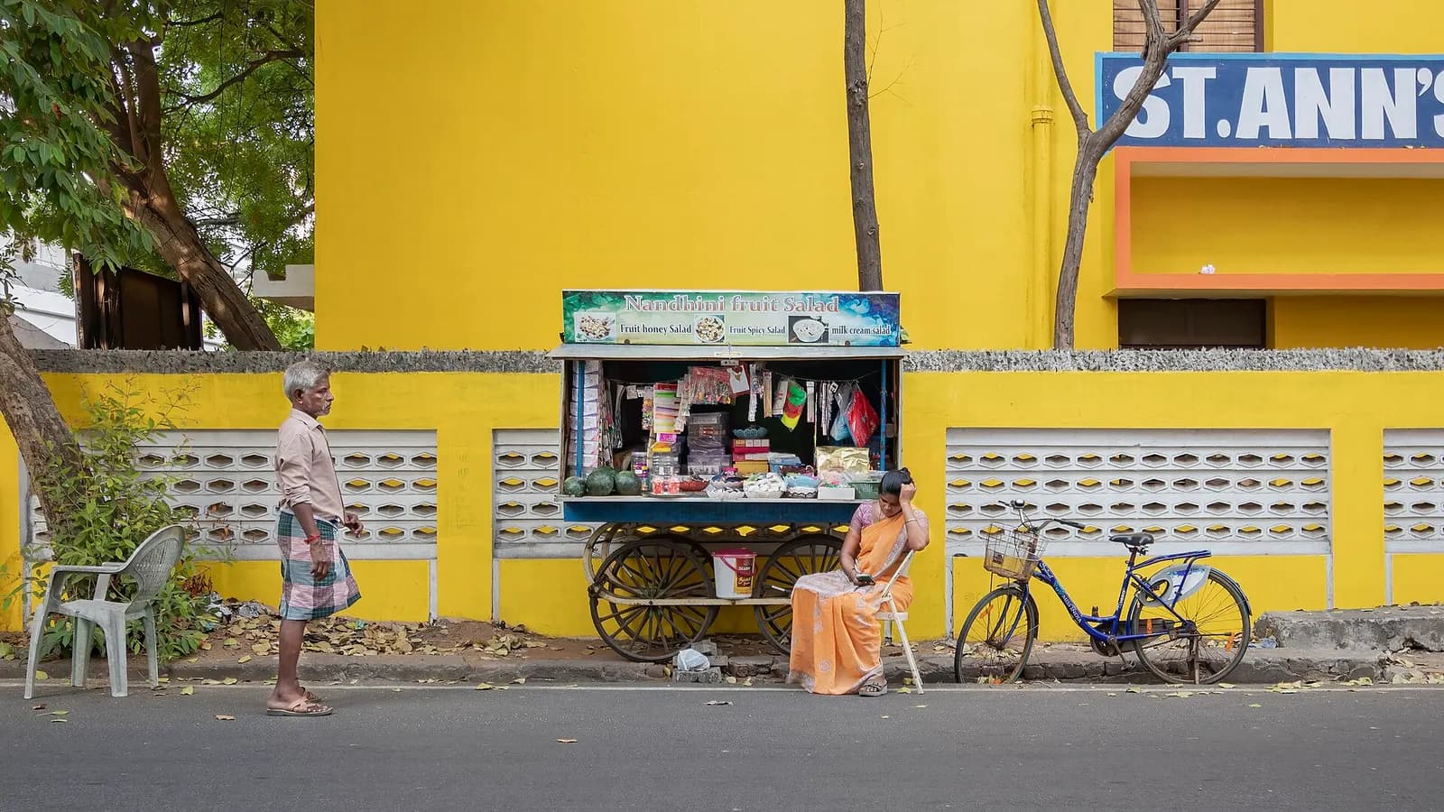 A small roadside stall in front of a yellow wall on a street in Puducherry town