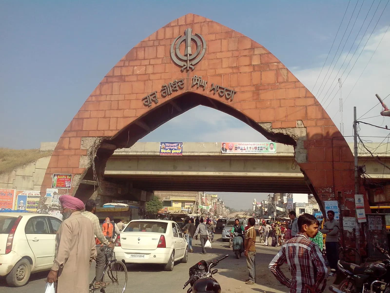 Busy road under the entrance arch at Sahnewal on the edge of Ludhiana, with cars, cyclists and shops