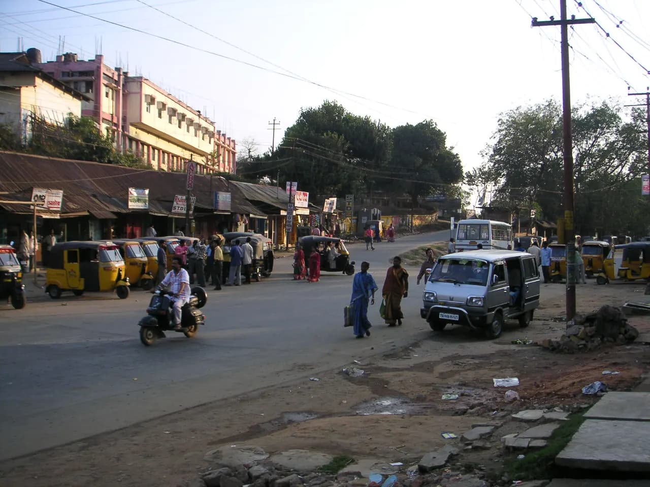 Auto-rickshaws, a scooter and pedestrians on a street lined with shops and offices in Agartala