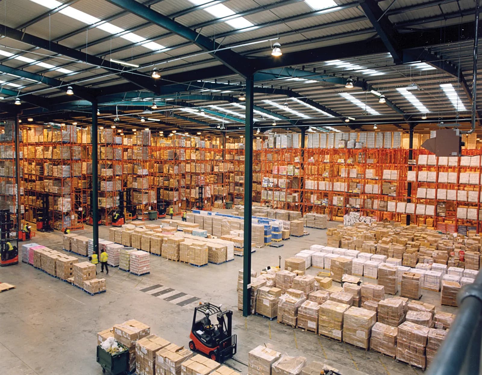 Large warehouse with tall pallet racks, stacked cartons and a forklift