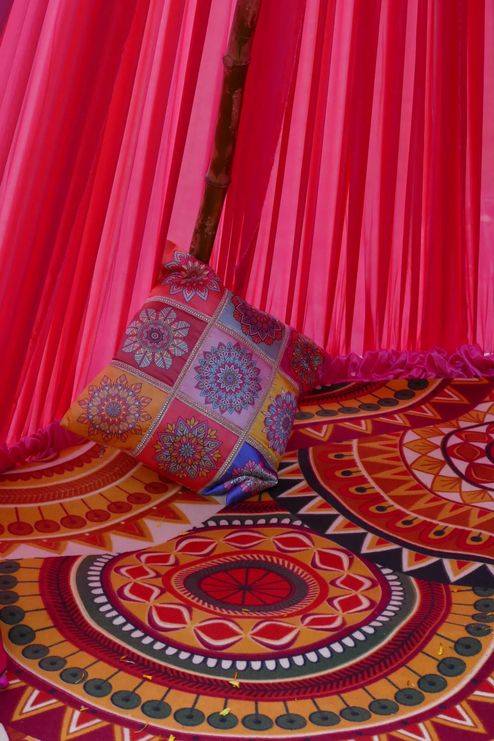 Pink fabric tent with a printed cushion and patterned floor covering set up for a haldi ceremony in South India