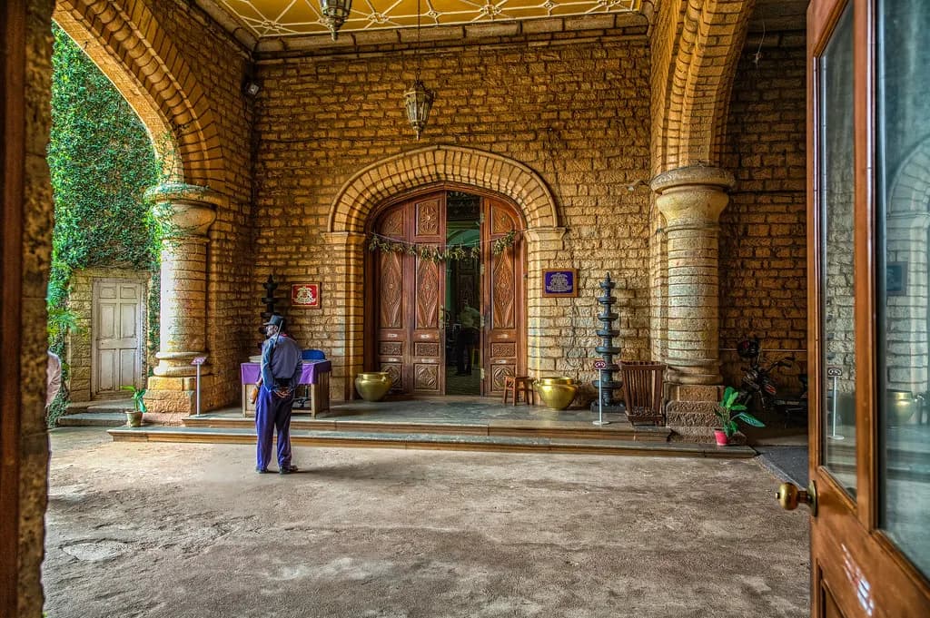 A uniformed security guard standing in the stone-arched entrance hall of Bangalore Palace