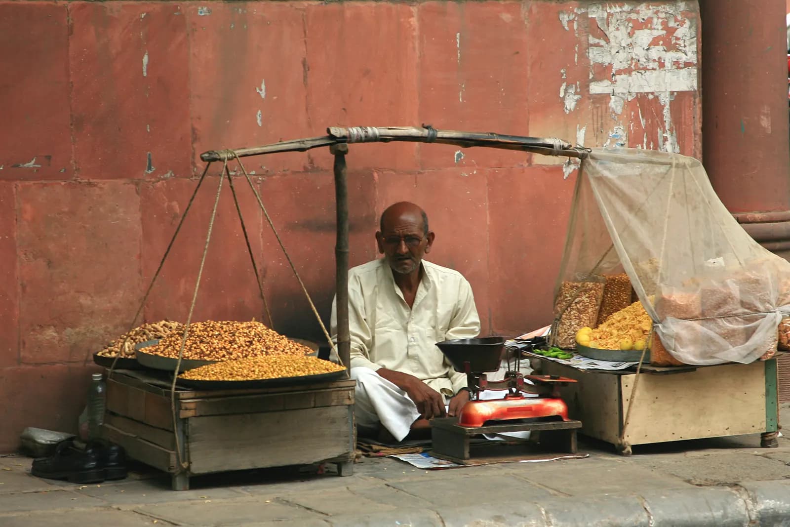 A namkeen seller with a hanging balance scale and trays of roasted snacks on the pavement at Khan Market, Delhi