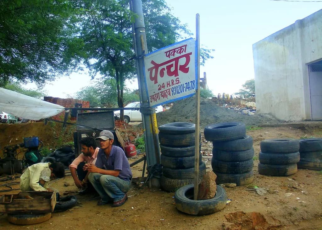 A small roadside tyre-puncture repair shop with stacked tyres and a hand-painted sign