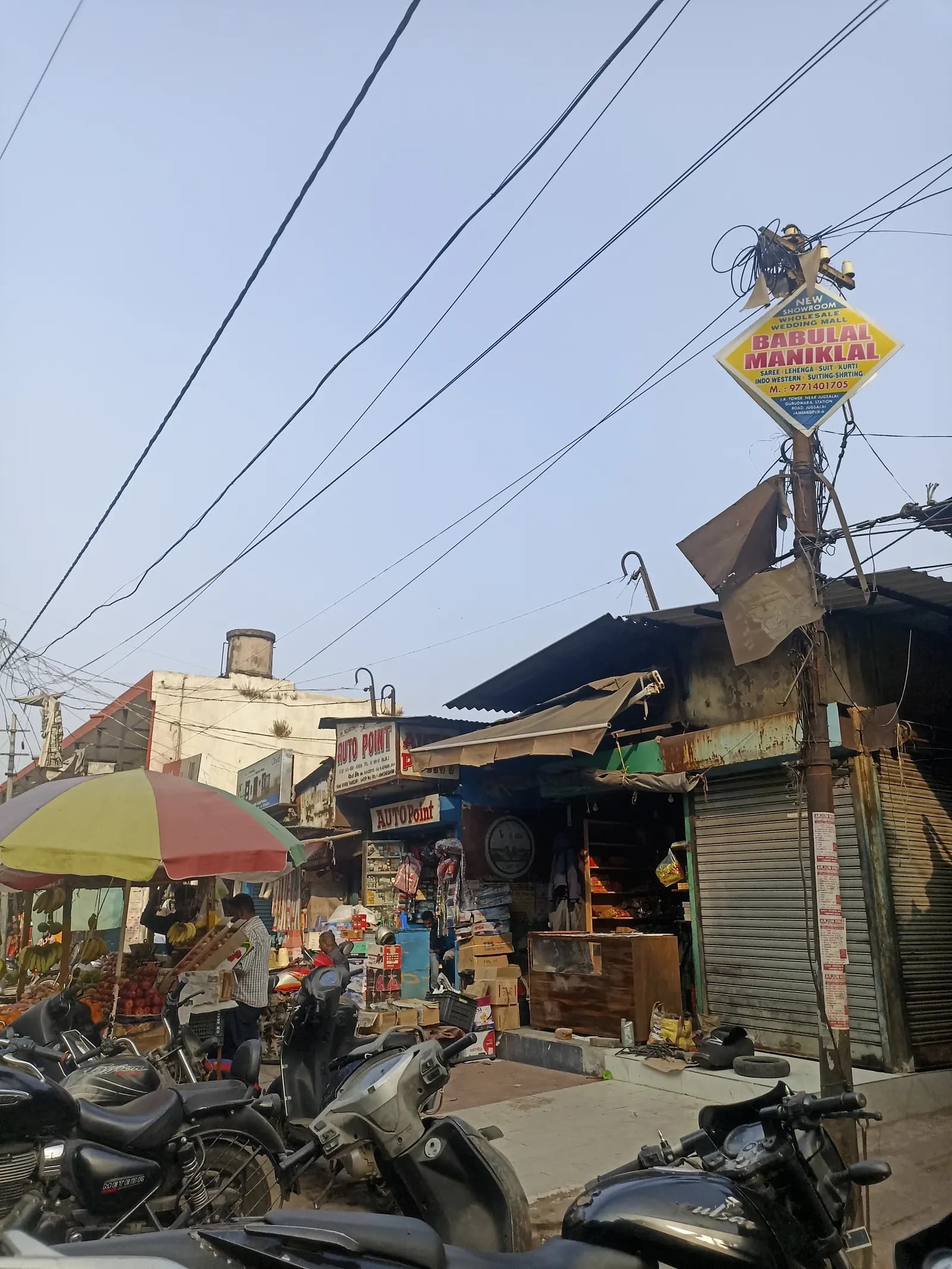 Small shops with shutters and awnings under old buildings in a local market in Jamshedpur, with motorcycles parked in front