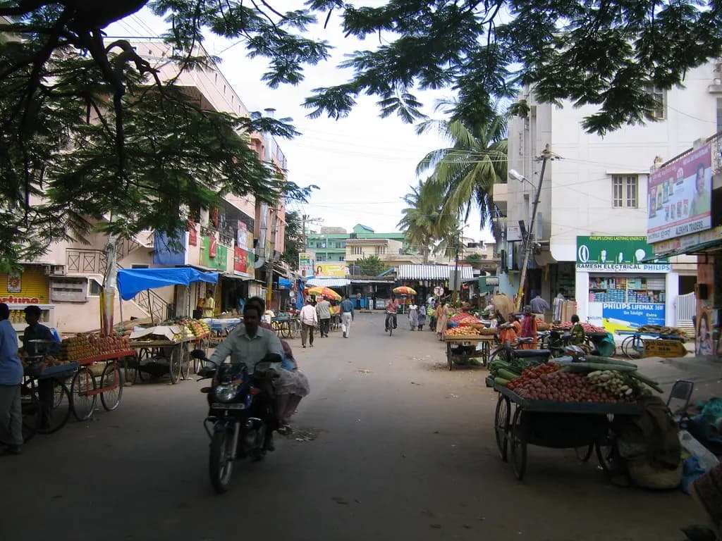 A street in Tippasandra, Bengaluru, lined with small shops, fruit and vegetable carts and two-wheelers