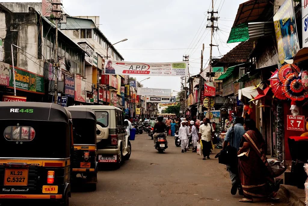 A busy market street in Thiruvananthapuram with shops, autorickshaws and shoppers