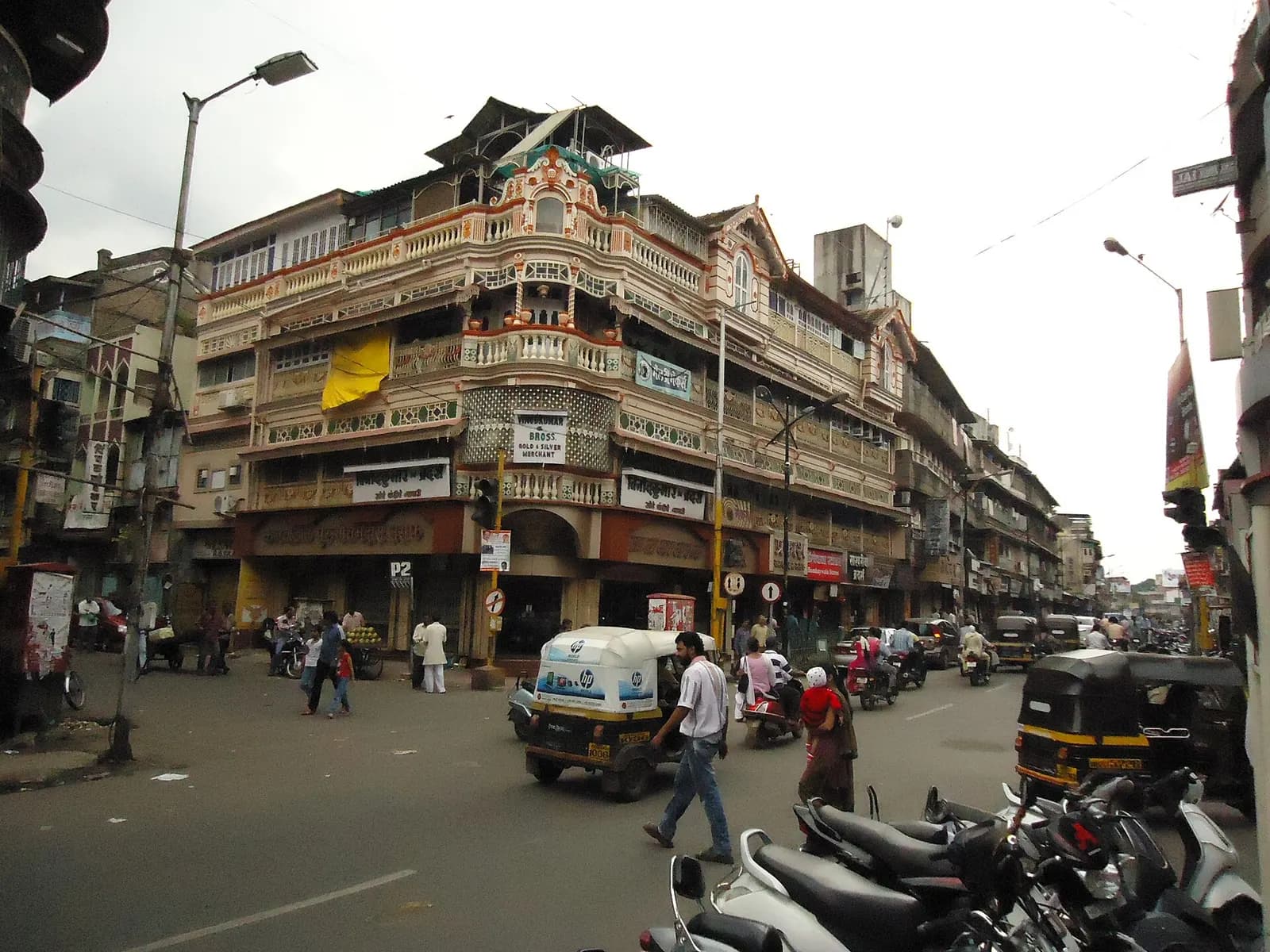 A corner building on Laxmi Road, Pune, with shops on the ground floor and auto-rickshaws in the street