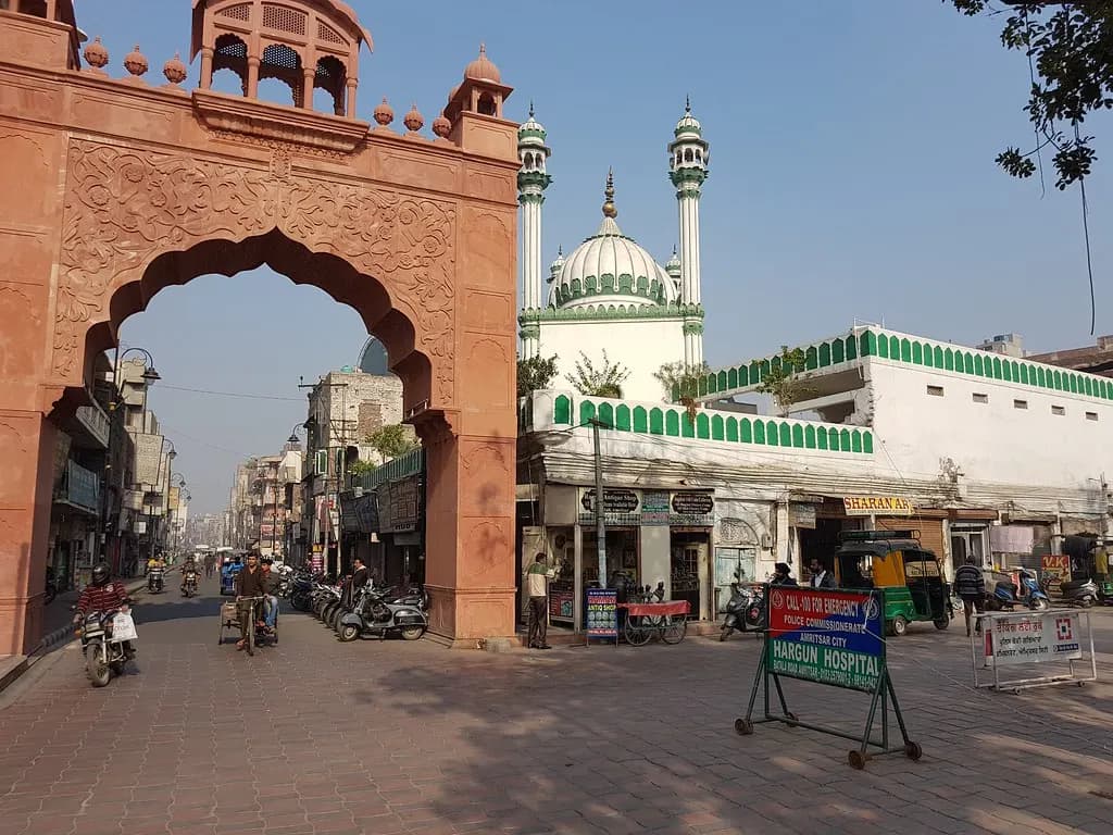 The red sandstone entrance arch at the end of Hall Bazaar in Amritsar, with shops and scooters along the street