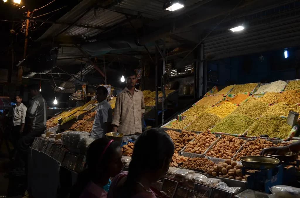 A brightly lit dry fruit and namkeen shop with heaped trays at Hazratganj market in Lucknow at night