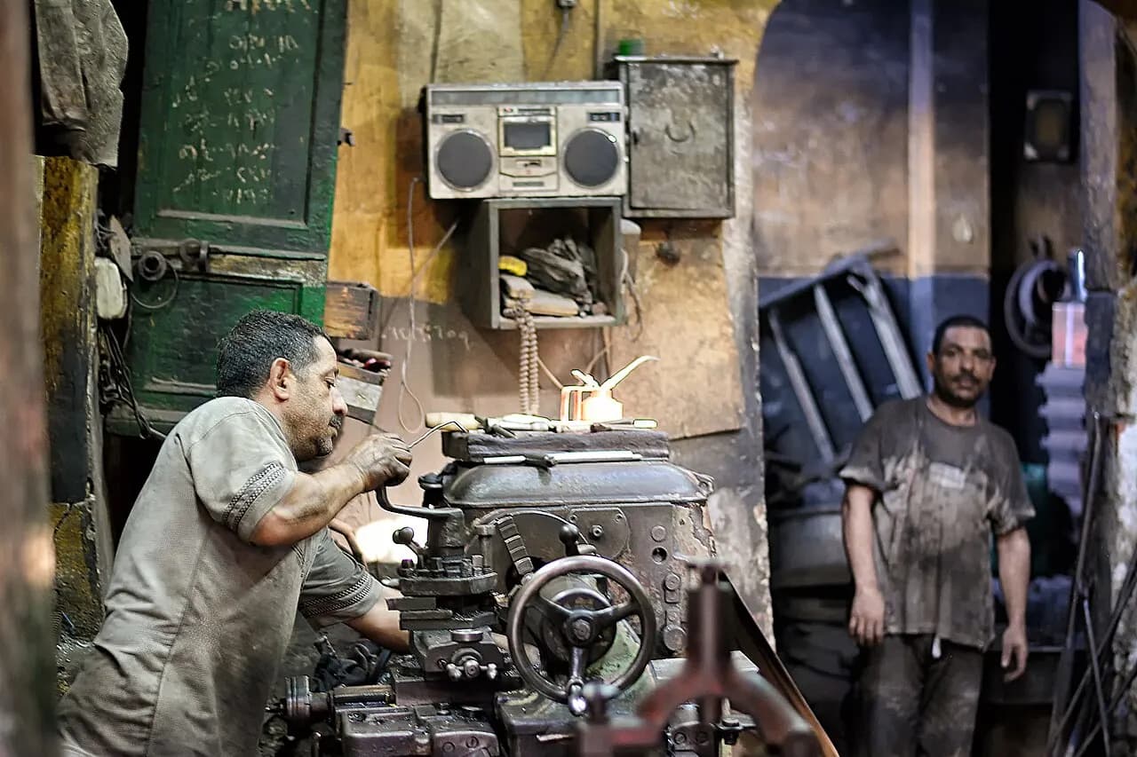 Machinists operating a heavy lathe in a small engineering workshop