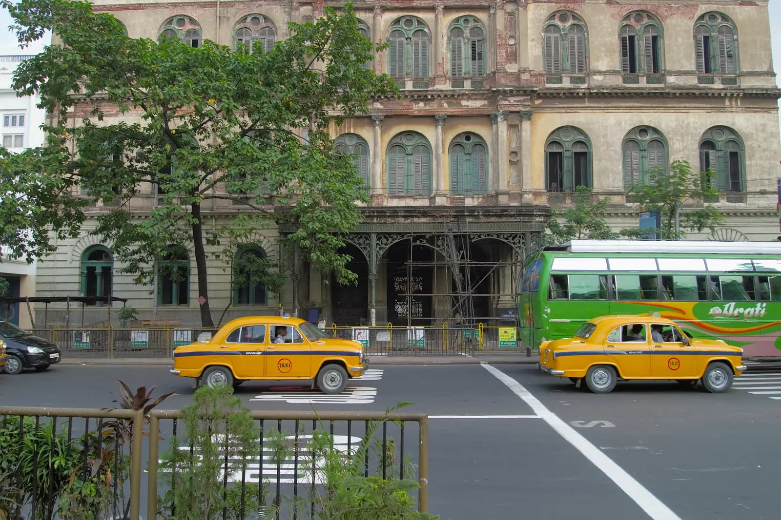 Two yellow Ambassador taxis on a street in Kolkata in front of a heritage building