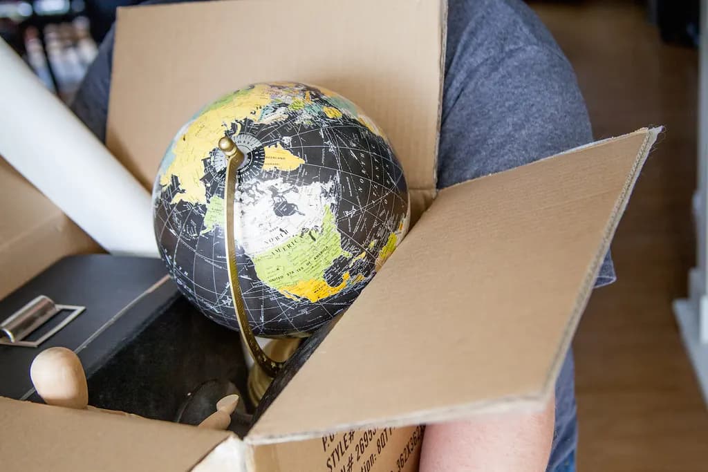 Hands packing a small globe and other items into an open cardboard shipping box