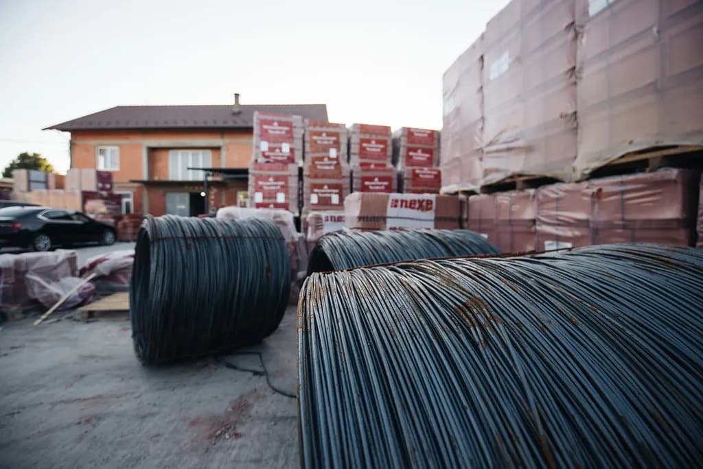 Coils of steel wire and wrapped pallets of building material stacked in a supply yard
