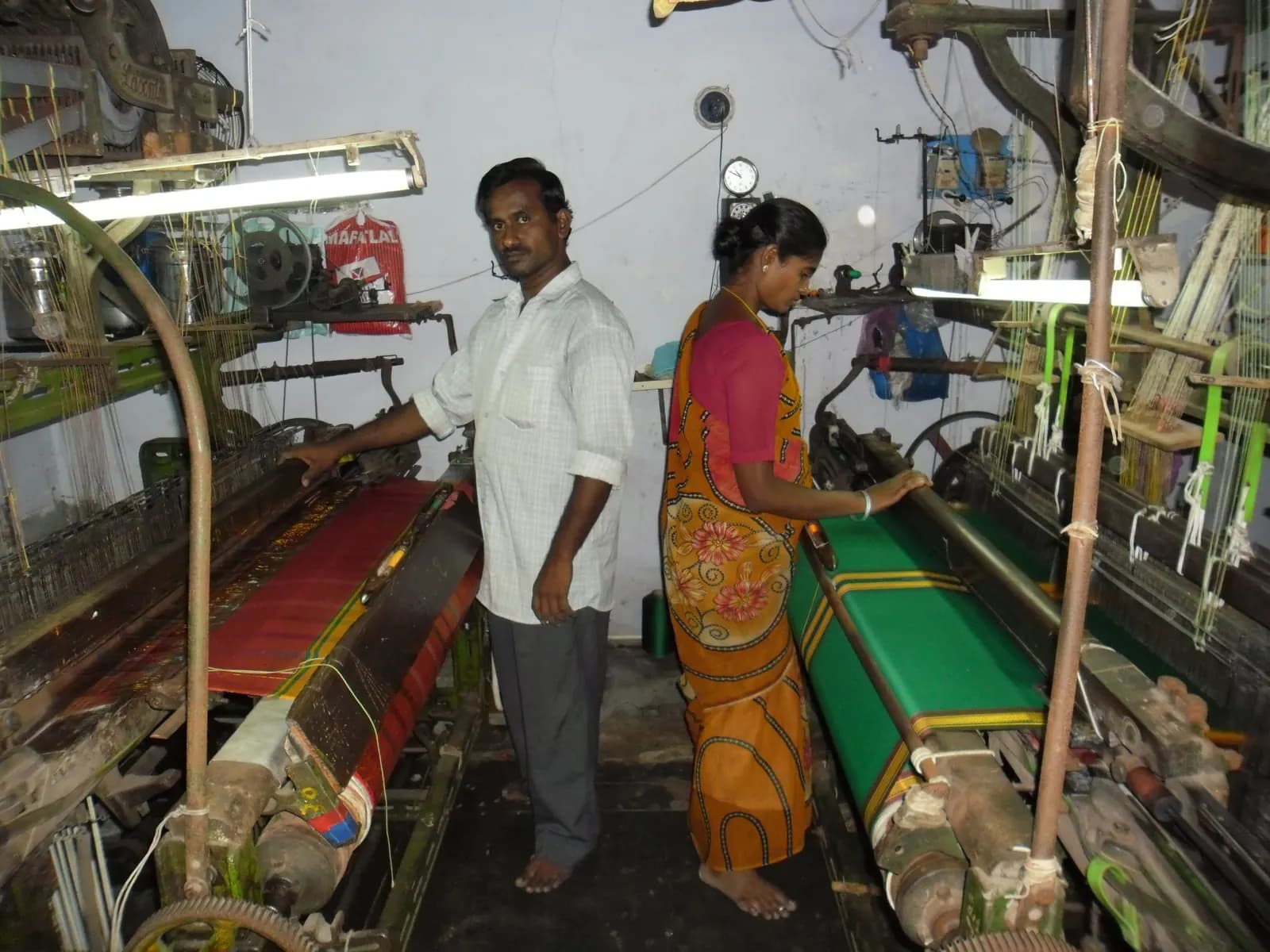 Two weavers tending power looms producing sari fabric in a small powerloom unit in Tamil Nadu