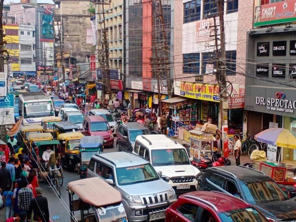 A busy commercial street at Nazirpatty in Silchar lined with shops, autorickshaws and cars