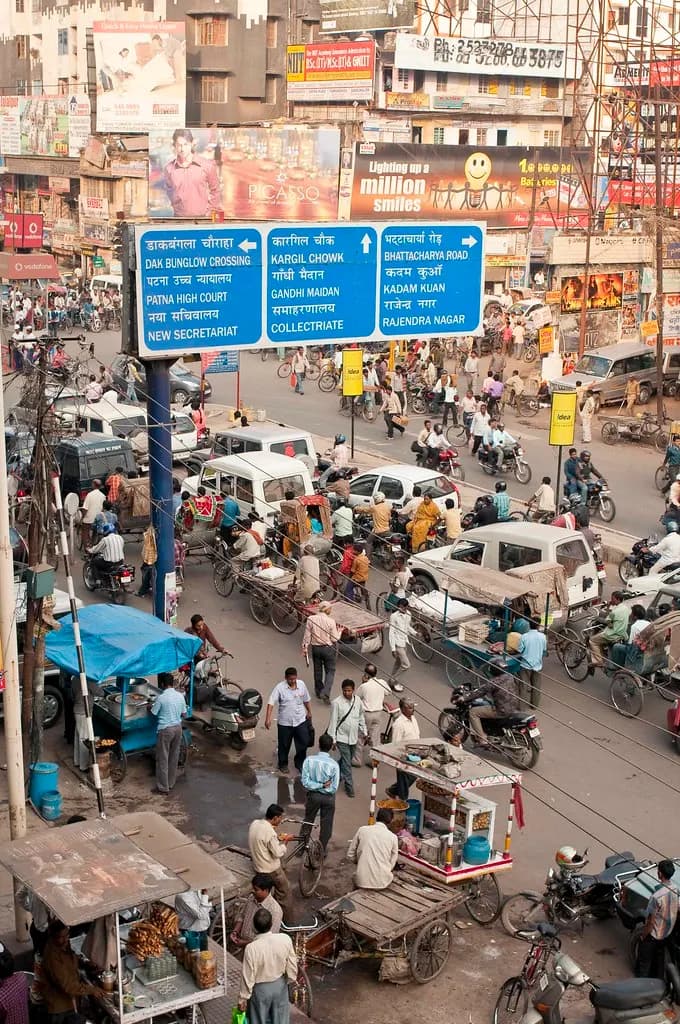 A busy Patna crossing with road signs, shop signboards, cycle-rickshaws and street vendors' carts